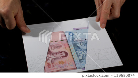 Money is placed inside an envelope with hands showing cash from different currencies Money is placed inside an envelope with hands showing cash from different currencies 139680874