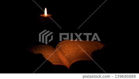 Candlelight illuminates an open book in a dark setting during the evening hours Candlelight illuminates an open book in a dark setting during the evening hours 139680889