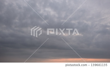 A cloudy gray sky fills the frame, with a hint of warm pink and orange light peeking through at the bottom. The clouds are dense and layered, giving the scene a feeling of an impending storm. A cloudy gray sky fills the frame, with a hint of warm pink and orange light peeking through at the bottom. The clouds are dense and layered, giving the scene a feeling of an impending storm. 139681135