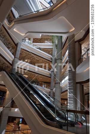 Luxury mall with atrium, multi-story corridors, and escalator interior featuring hanging plants on columns. 139681256
