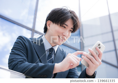 一位英俊瀟灑的商人站在建築物的室外樓梯上,用智慧型手機敲擊螢幕。 一位英俊瀟灑的商人站在建築物的室外樓梯上,用智慧型手機敲擊螢幕。 139681335