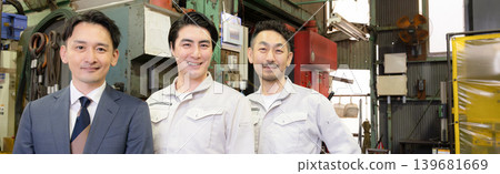 A team of three salesmen in work clothes and suits working on the factory floor of a manufacturing plant; a banner for a small business featuring smiling faces looking directly at the camera. A team of three salesmen in work clothes and suits working on the factory floor of a manufacturing plant; a banner for a small business featuring smiling faces looking directly at the camera. 139681669