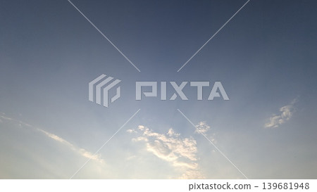 A clear blue sky deepens toward the top, grading down to a bright haze near the bottom horizon. A few scattered, illuminated white cumulus clouds drift in the lower center of the frame. A clear blue sky deepens toward the top, grading down to a bright haze near the bottom horizon. A few scattered, illuminated white cumulus clouds drift in the lower center of the frame. 139681948