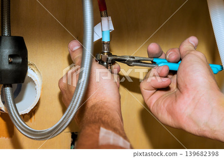 Worker repairs plumbing under sink using tools in kitchen setting Worker repairs plumbing under sink using tools in kitchen setting 139682398