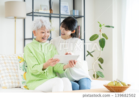 Senior parent and child using a tablet in the living room Senior parent and child using a tablet in the living room 139682502