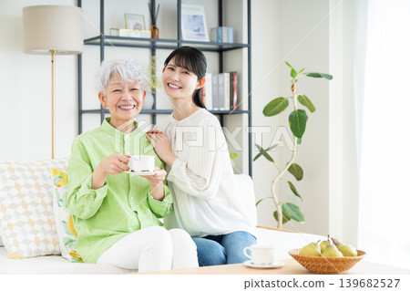 一位年長的母親和她中年的女兒在客廳喝咖啡。 一位年長的母親和她中年的女兒在客廳喝咖啡。 139682527