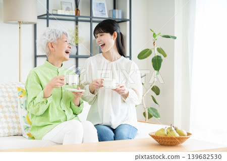 A senior mother and her middle-aged daughter drinking coffee in the living room. A senior mother and her middle-aged daughter drinking coffee in the living room. 139682530