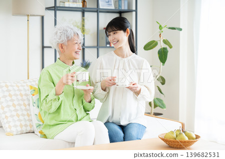 A senior mother and her middle-aged daughter drinking coffee in the living room. A senior mother and her middle-aged daughter drinking coffee in the living room. 139682531
