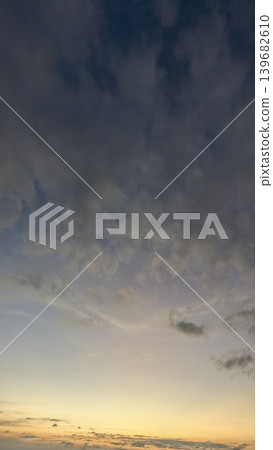 A peaceful sky with light, fluffy clouds. The colors shift from a cool, dusky gray to a hint of pink and yellow at the bottom. A few small, darker clouds add texture to the scene. A peaceful sky with light, fluffy clouds. The colors shift from a cool, dusky gray to a hint of pink and yellow at the bottom. A few small, darker clouds add texture to the scene. 139682610