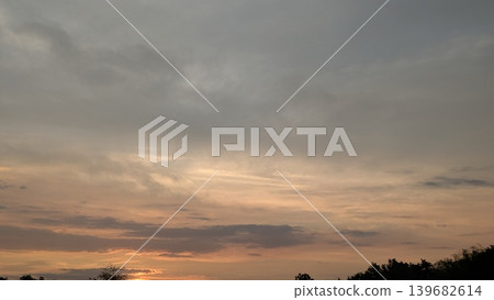 A vast sky is filled with a mix of dark clouds and vibrant, glowing orange and pink hues from a sunset, with a silhouette of trees on the horizon below. The scene is dramatic yet peaceful. 139682614