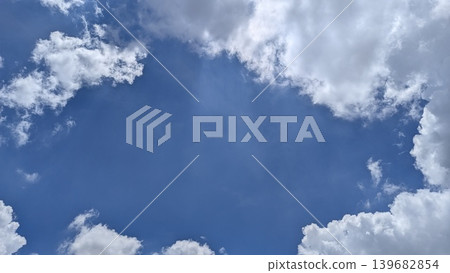 Fluffy white clouds frame a bright, deep blue sky, creating a natural window or copy space in the center. A classic skyscape abstract background for overlay text or design elements. Fluffy white clouds frame a bright, deep blue sky, creating a natural window or copy space in the center. A classic skyscape abstract background for overlay text or design elements. 139682854