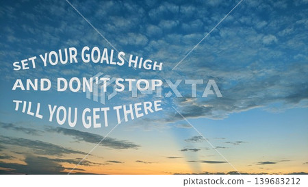 An empowering quote SET YOUR GOALS HIGH AND DON'T STOP TILL YOU GET THERE displayed against a beautiful blue and orange sunset sky with scattered clouds. 139683212