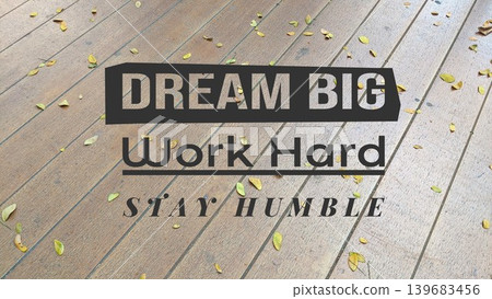A motivational message DREAM BIG, Work Hard, STAY HUMBLE overlaid on a wooden floor with scattered leaves, inspiring ambition, effort, and modesty. A motivational message DREAM BIG, Work Hard, STAY HUMBLE overlaid on a wooden floor with scattered leaves, inspiring ambition, effort, and modesty. 139683456