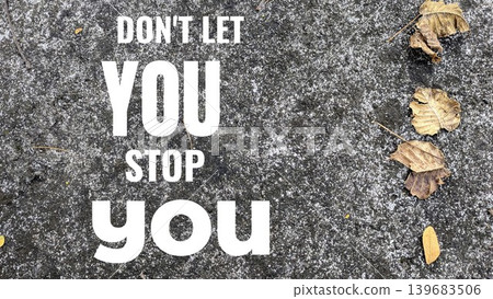 A bold and direct motivational quote, Don't let you stop you, displayed on a textured grey concrete surface with scattered dry leaves. 139683506