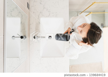 A woman drying her hair with a hair dryer Beauty image 139684419