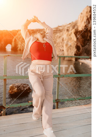Woman coastline relaxation standing on a wooden pier with arms raised and head back enjoying the golden sunset over the sea Woman coastline relaxation standing on a wooden pier with arms raised and head back enjoying the golden sunset over the sea 139684552