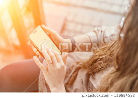 Smartphone mobile technology woman using cellular phone in bright sunny outdoor environment with warm golden lens flare Smartphone mobile technology woman using cellular phone in bright sunny outdoor environment with warm golden lens flare 139684558