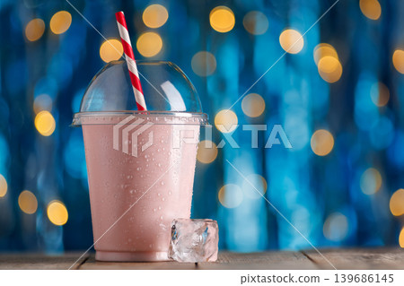 Strawberry milkshake in disposable plastic cup with condensation and red and white striped straw on wooden surface, vibrant bokeh background, refreshing summer treat Strawberry milkshake in disposable plastic cup with condensation and red and white striped straw on wooden surface, vibrant bokeh background, refreshing summer treat 139686145