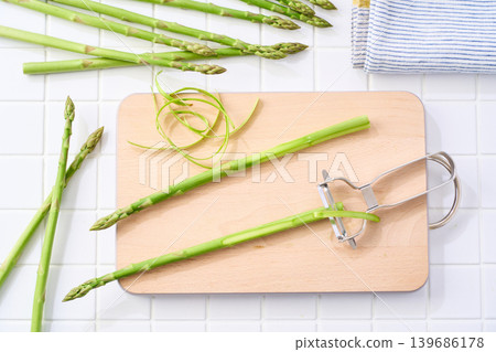 A scene showing the preparation of green asparagus by peeling it with a vegetable peeler. A scene showing the preparation of green asparagus by peeling it with a vegetable peeler. 139686178