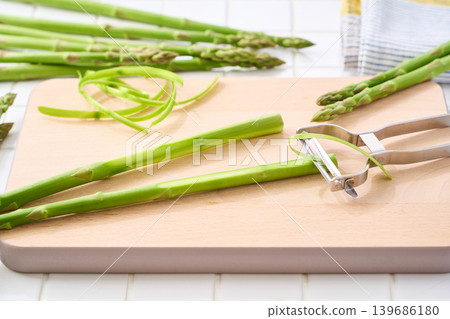 A scene showing the preparation of green asparagus by peeling it with a vegetable peeler. A scene showing the preparation of green asparagus by peeling it with a vegetable peeler. 139686180