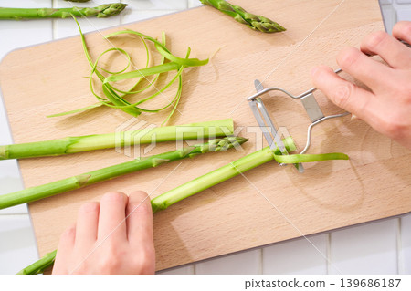 Green asparagus: Peeling the skin with a peeler (hands during preparation) Green asparagus: Peeling the skin with a peeler (hands during preparation) 139686187