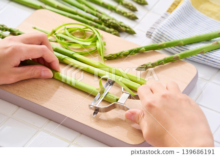 Green asparagus: Peeling the skin with a peeler (hands during preparation) Green asparagus: Peeling the skin with a peeler (hands during preparation) 139686191
