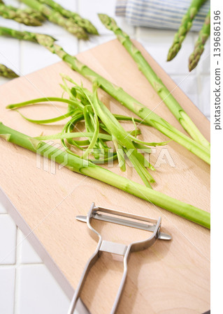 A scene showing the preparation of green asparagus by peeling it with a vegetable peeler. A scene showing the preparation of green asparagus by peeling it with a vegetable peeler. 139686196