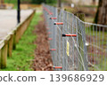 Electric wire fence with wooden posts and orange plastic insulators in park area. Outdoor security barrier 139686929