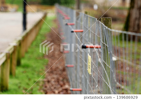 Electric wire fence with wooden posts and orange plastic insulators in park area. Outdoor security barrier 139686929