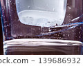Purified drinking water flowing from a carbon filter cartridge in a household plastic pitcher on a dark background  139686932