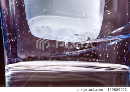 Purified drinking water flowing from a carbon filter cartridge in a household plastic pitcher on a dark background  139686932