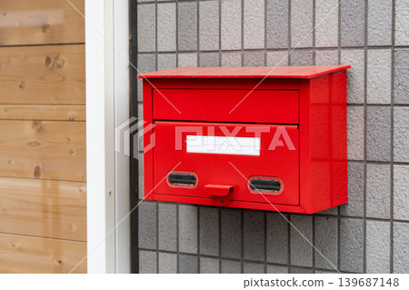 A red mailbox installed on the exterior wall of a house. A red mailbox installed on the exterior wall of a house. 139687148