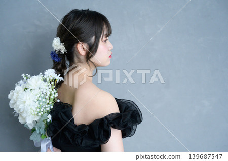 一位身穿黑色洋裝的日本女子手捧花束，背景為灰色。 139687547