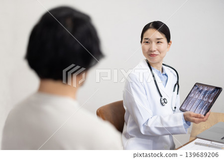 A Japanese female doctor in a white coat examines a male patient. A Japanese female doctor in a white coat examines a male patient. 139689206
