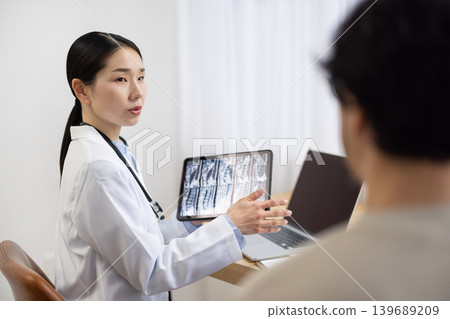 A Japanese female doctor in a white coat examines a male patient. A Japanese female doctor in a white coat examines a male patient. 139689209