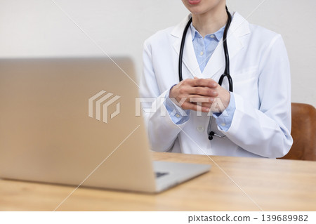 A close-up of the hands of a Japanese female doctor in a white coat making an online call on her computer. A close-up of the hands of a Japanese female doctor in a white coat making an online call on her computer. 139689982