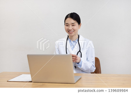 Japanese female doctor in a white coat making an online call on her computer 139689984