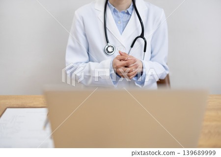 A close-up of the hands of a Japanese female doctor in a white coat making an online call on her computer. A close-up of the hands of a Japanese female doctor in a white coat making an online call on her computer. 139689999