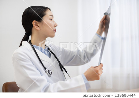 A Japanese female doctor in a white coat looking at X-ray images. A Japanese female doctor in a white coat looking at X-ray images. 139690444