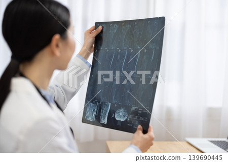 A Japanese female doctor in a white coat looking at X-ray images. A Japanese female doctor in a white coat looking at X-ray images. 139690445