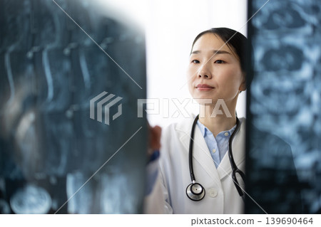 A Japanese female doctor in a white coat looking at X-ray images. 139690464