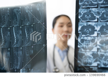 A Japanese female doctor in a white coat looking at X-ray images. 139690466