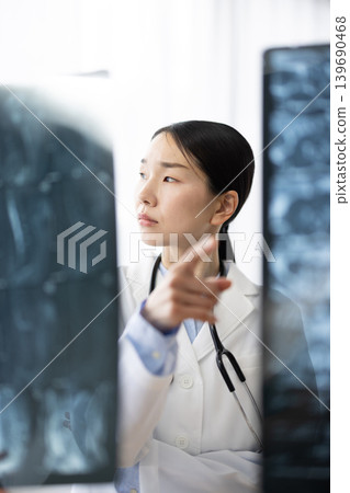 A Japanese female doctor in a white coat looking at X-ray images. A Japanese female doctor in a white coat looking at X-ray images. 139690468