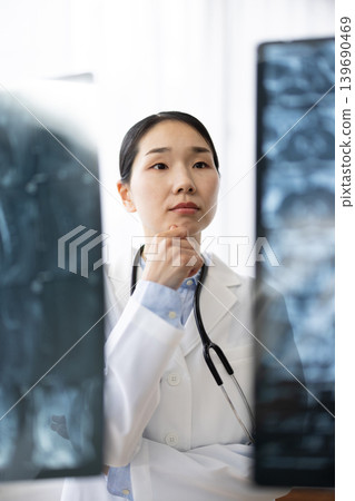A Japanese female doctor in a white coat looking at X-ray images. 139690469