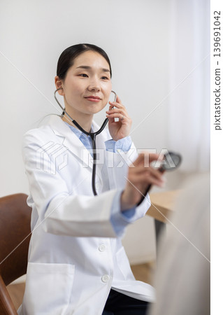 一位身穿白大褂的日本女醫生正在用聽診器為一位女病人進行檢查。 139691042
