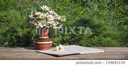 Camomiles in the vase and book 139693139