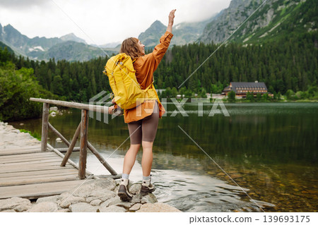 Travel Slovakia, Europe. Tourist with a yellow backpack stands against the backdrop of alpine lake. Travel Slovakia, Europe. Tourist with a yellow backpack stands against the backdrop of alpine lake. 139693175