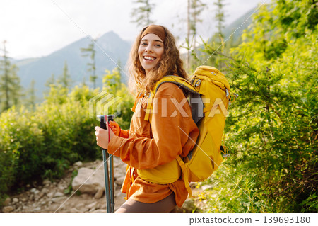 Young woman traveler hiking poles on trail among the mountains. Hiking. Active lifestyle. Young woman traveler hiking poles on trail among the mountains. Hiking. Active lifestyle. 139693180