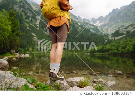 Travel Slovakia, Europe. Tourist with a yellow backpack stands against the backdrop of alpine lake. Travel Slovakia, Europe. Tourist with a yellow backpack stands against the backdrop of alpine lake. 139693194