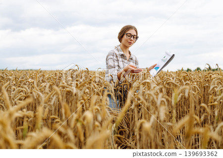 A young woman agronomist in a wheat field with a tablet in her hand checks the field. A young woman agronomist in a wheat field with a tablet in her hand checks the field. 139693362